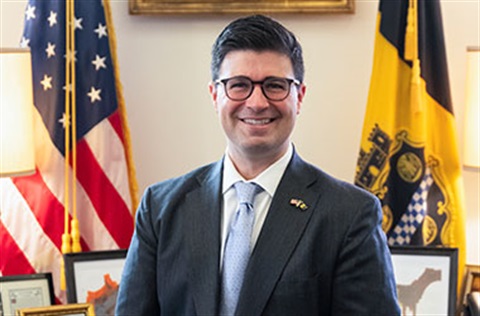 Mayor Corey O'Connor - Standing between American and City flags in office.