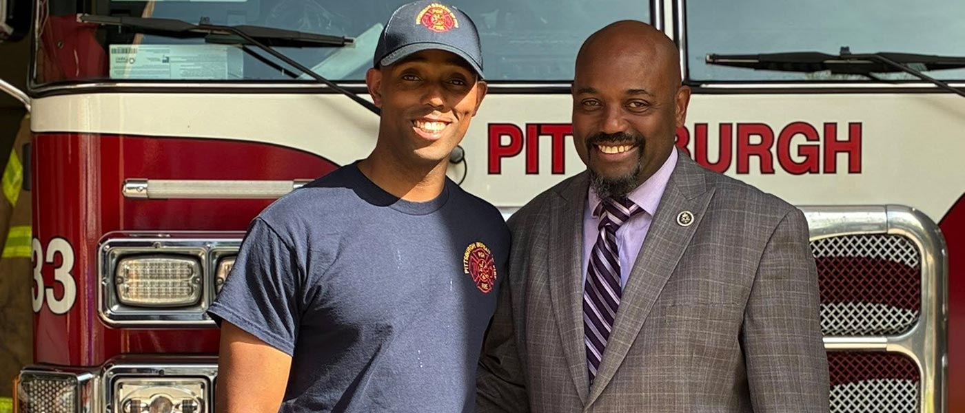 Firefighter and gentleman standing in front of Fire Engine.