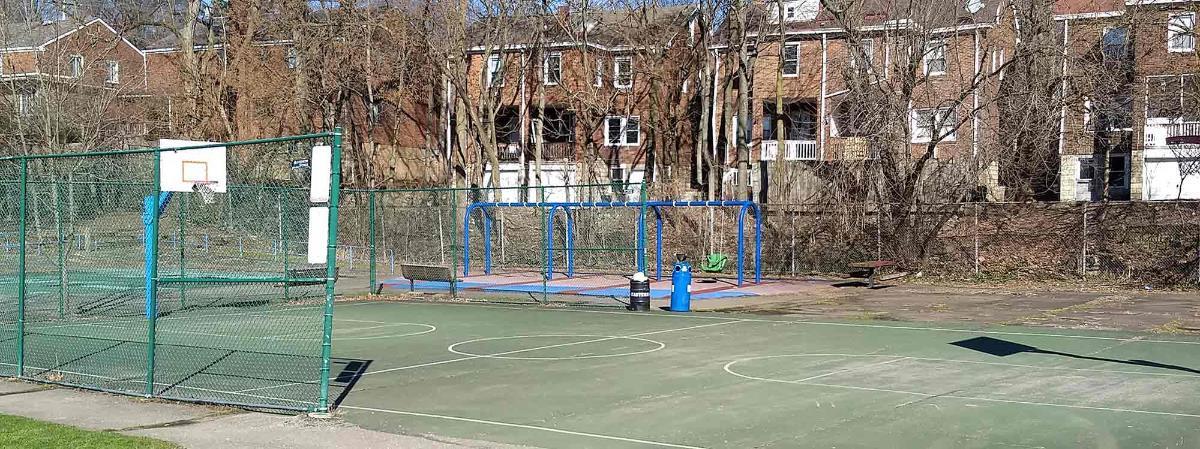 Wide photo shot of old basketball court and swing set.
